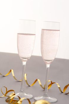 Celebrating with two elegant flutes of sparkling pink champagne with twirled gold party streamers for a special romantic occasion