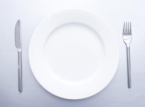 Plain simple place setting with empty white plate flanked by a silver knife and for viewed from overhead