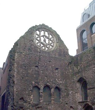 Remnants of a rose window in an old ruined historic stone church with boarded up windows under a cloudy sky