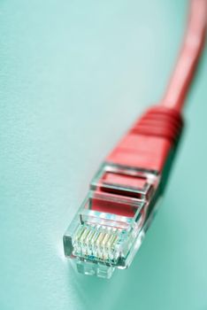A close up of a red ethernet network cable plug on isolated on a plain blue background.