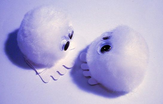 Pair of round soft fluffy little toys with big eyes and four toes photographed in purple light on a white background from above