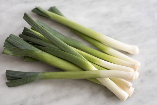 A close up of several fresh, green leeks on a marble bench top.
