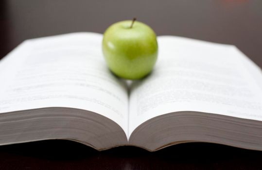 Fresh green apple balanced on the open pages of a textbook or novel in an education and learning or relaxation and reading concept