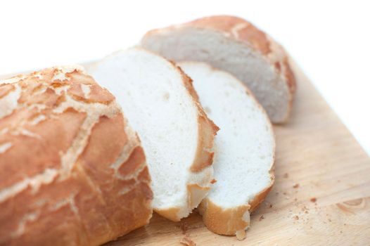 Sliced fresh white crusty bread on a wooden bread board over a white background
