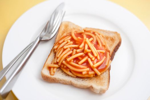Cheap quick snack of canned spaghetti in tomato sauce on a slice of white toast served on a plate