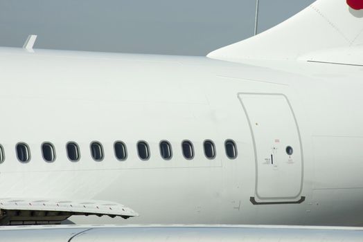 A close up of passenger windows and exit door on a large commercial airline plane.