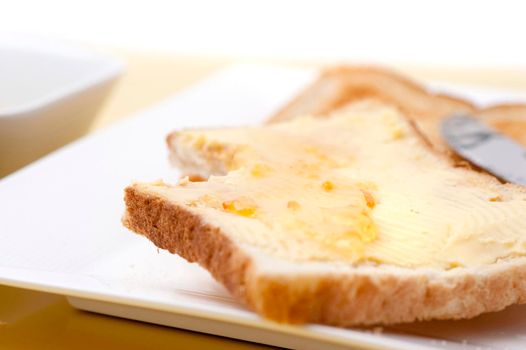 Breakfast serving on a plate of a slice of buttered toast topped with marmalade with a single bite taken out of it