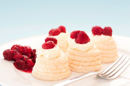Decorative twirled meringues filled with whipped cream and topped with fresh raspberries served on a plate with a fork