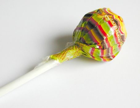Close-up of a delicious lollipop or lolly wrapped in colorful plastic, with white stick, with copy space on grey