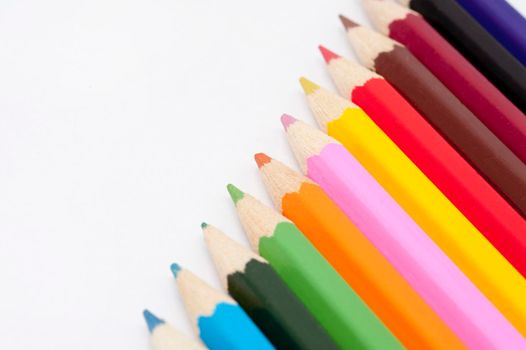 Row of coloured pencil crayons in the colours of the rainbow in a diagonal line with copyspace on a white background