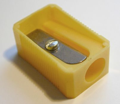 Simple yellow plastic pencil sharpener with a close up view on the blade at the top for school or office supplies