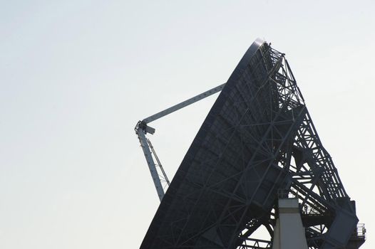 Silhouette of a parabolic dish satellite antenna in side view over a grey sky with copy space in a communications concept