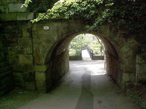 Pass under the arch through an old thick stone wall with green foliage