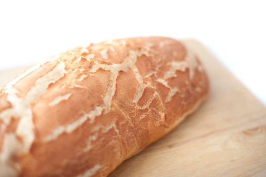 Close up view with shallow dof of a freshly baked crusty loaf of white bread on a wooden bread board over white