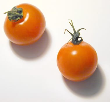 Two ripe red cherry tomatoes with green stalks viewed high angle on white with shadows in square format