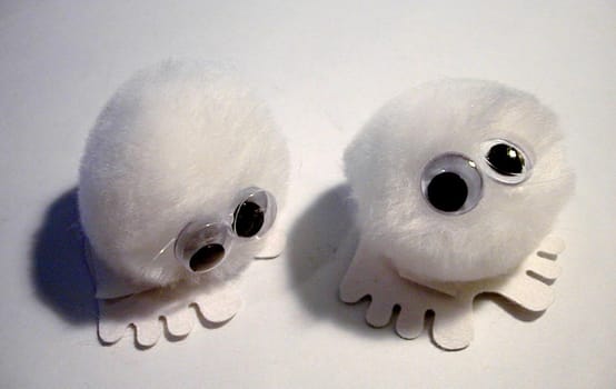 Overhead view of cute fluffy white puff balls with felt feet and glued on eyes