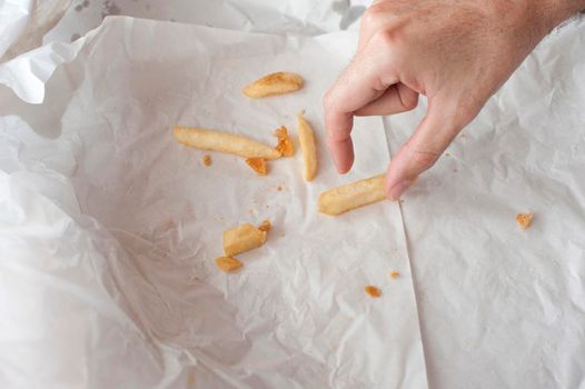 Man eating takeaway French fries reaching out his hand to take the last few left on a piece of crumpled white paper
