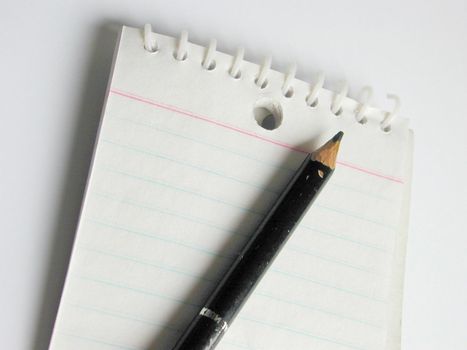 Close up view of short black pencil placed on a blank lined notepad against a white background