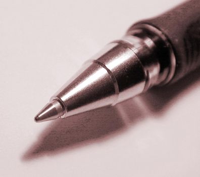 Close up of the silver metal nib of a ballpoint pen casting a shadow on a white background, square format