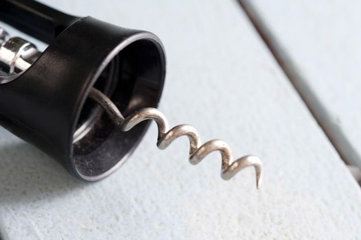 Close up on the sharp metal spiral on a corkscrew bottle opener over a white wood background with copy space