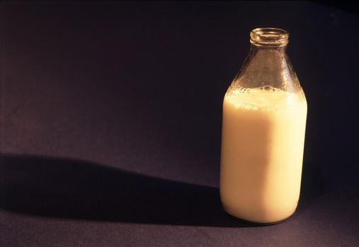 Traditional clear glass bottle of delicious fresh creamy cows milk on a black background with copyspace