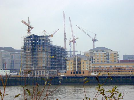 Waterfront urban construction of high-rise buildings surrounded by lots of industrial cranes viewed over the water on a misty day