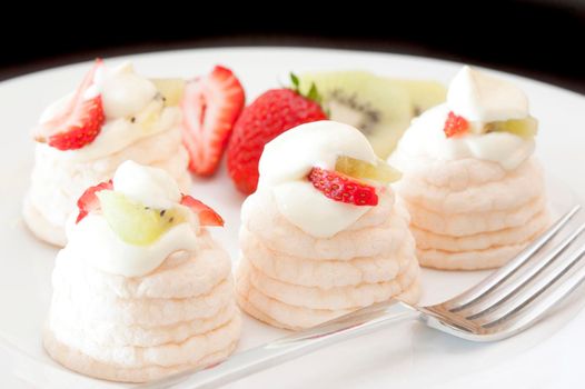Individual meringue cases filled with whipped cream and topped with sliced fresh fruit including strawberries and kiwi fruit