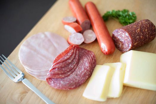 Nourishing German breakfast with a variety of cold spicy salami, ham and sausage served with portions of cheese on a wooden chopping board
