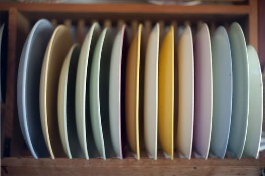 Selection of clean colourful dinner plates in a wooden rack mounted on a kitchen wall ready to be used to serve the food