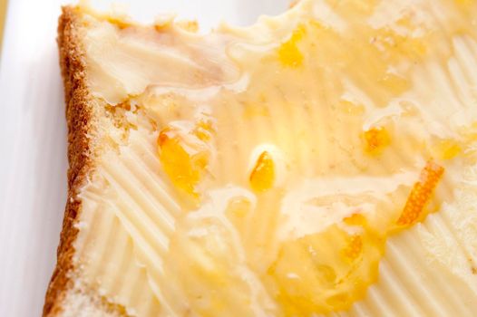 Slice of breakfast toast spread with butter and topped with marmalade or preserve