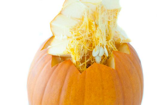 Decoratively cut fresh pumpkin with the cut portion lifted away to reveal the fibres and healthy pips inside over a white background