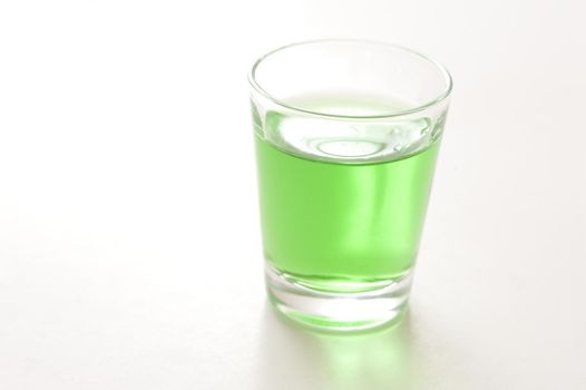 Shot glass filled with green absinthe liqueur prepared from herbs with a high alcohol content and potency