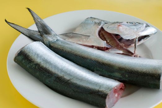 Preparing raw fish from the days fishing catch in the kitchen on a plate removing the head and tail and filleting the body