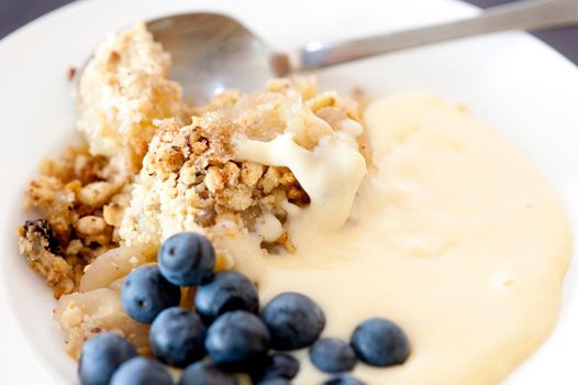 Serving of apple blackcurrent dessert with delicious crisp crumbly topping, a creamy sauce and fresh whole blackcurrents, close up view
