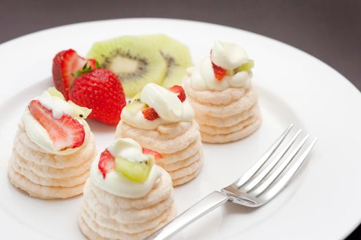 Meringue dessert with small individual meringues filled with cream and topped with kiwi fruit and strawberries