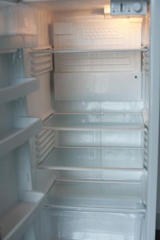 Open empty white refrigerator interior with shelves and compartments illuminated by the interior light showing it is on and connected to electricity