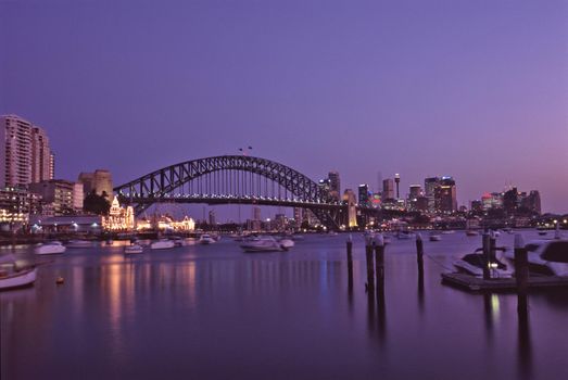 Purple sunset over Sydney Harbour Bridge, Australia on a tranquil summer evening with boat traffic and city lights in a transport and travel concept