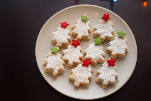 Plate of freshly baked homemade Christmas tree cookies decorated with colourful stars in green and red, high angle view