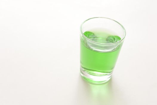 Glass of green absinthe liqueur, a potent beverage with a high alcohol content made with herbs, anise and wormwood, on a white background with copyspace