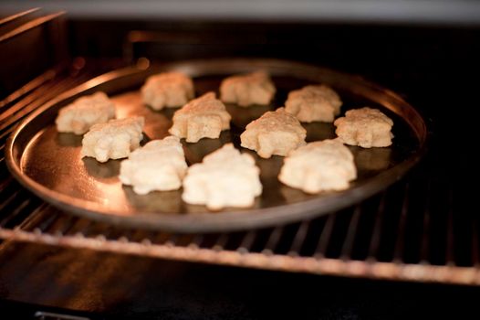 Christmas cookies in the shape of Christmas trees baking in the oven on a round baking tray