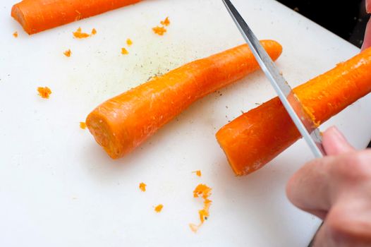 Man scraping carrots with a knife preparing them for cooking as a vegetable or as a salad ingredient
