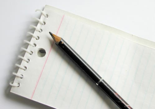 Pencil lying on a blank ruled spiral bound notepad viewed diagonally from above in a business or school concept