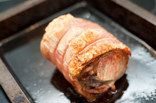 Crisp pork crackling on a roll of oven roasted pork in a grill pan