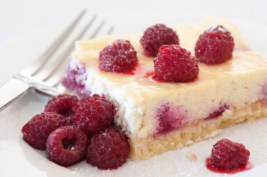 Raspberries on a slice of freshly baked ricotta cheesecake, close up view with a fork