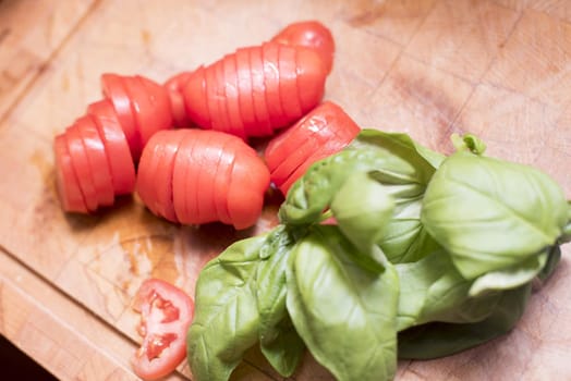 Sliced tomato and fresh basil on a chopping board ready for use in a salad, Mediterranean or Italian cooking
