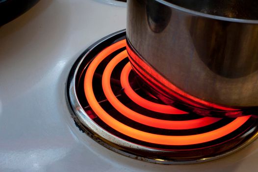 Cooking on the red hot spiral hotplate of an electric stove with a metal pot or saucepan