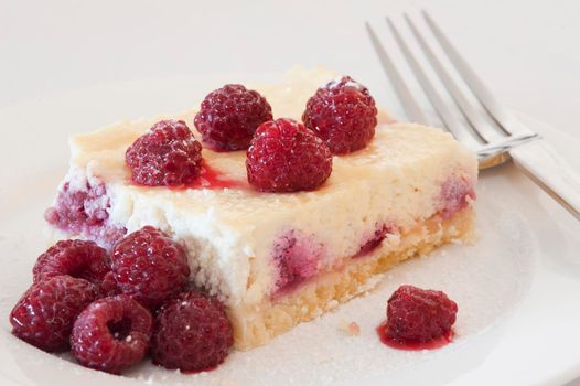 Portion of freshly baked ricotta cheesecake dessert topped with raspberries served with a fork