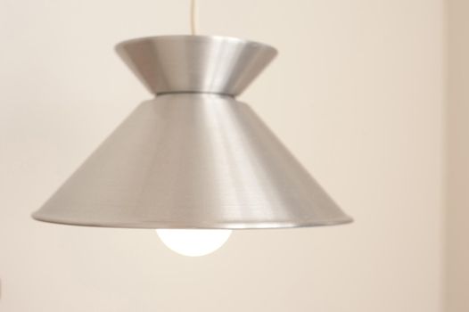 Hanging lamp with a silver metallic shade and glowing light bulb, close up view in an interior decor and power and energy concept