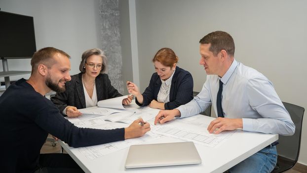 Four colleagues are discussing blueprints in a conference room in an office. Brainstorming of engineers and architects