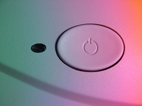 White oval power button with standby or power symbol viewed in graduated pink through green light